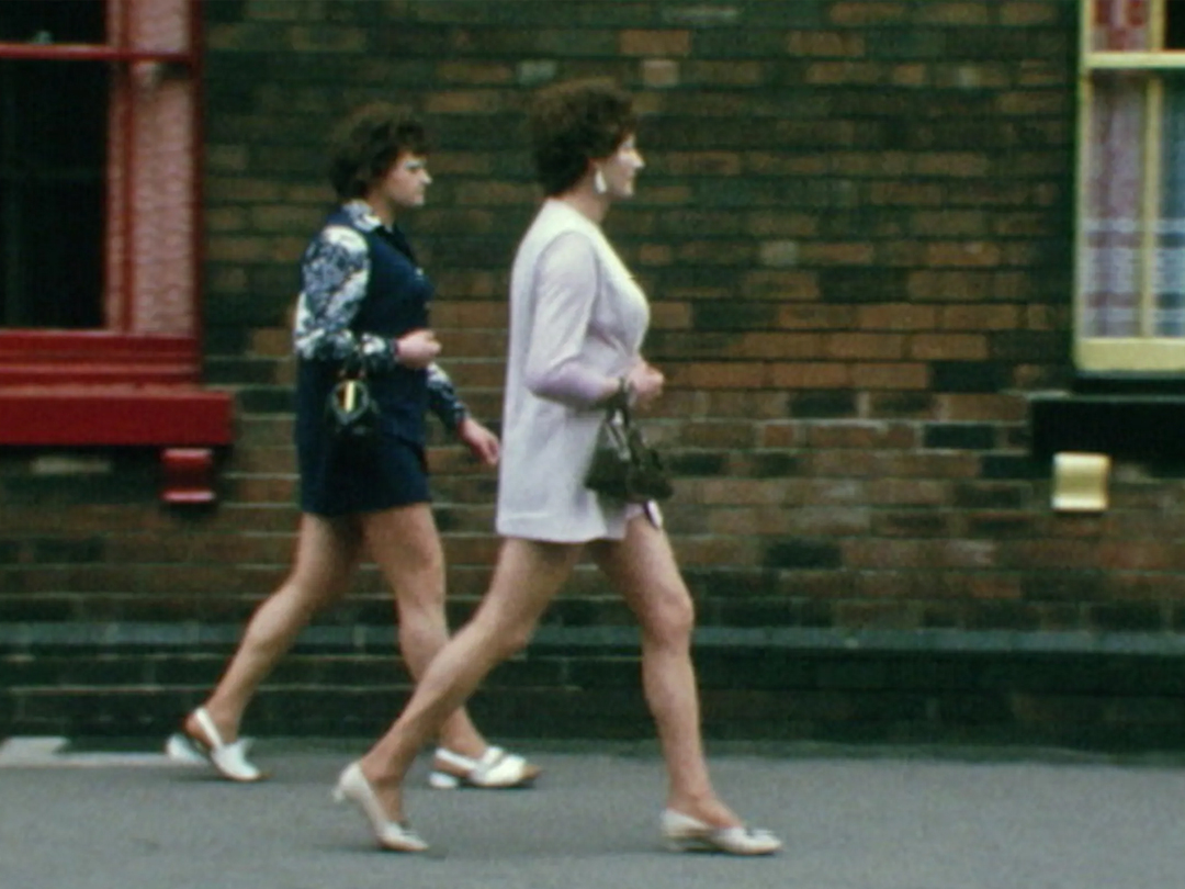 Two people walk along a brick-lined street, from Sheffield Transvestite Eviction.