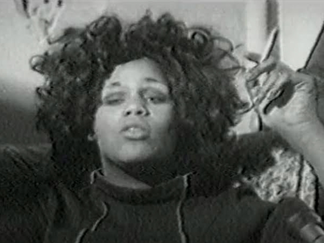 Black-and-white close-up of a person with curly hair speaking, from Transsexuals.